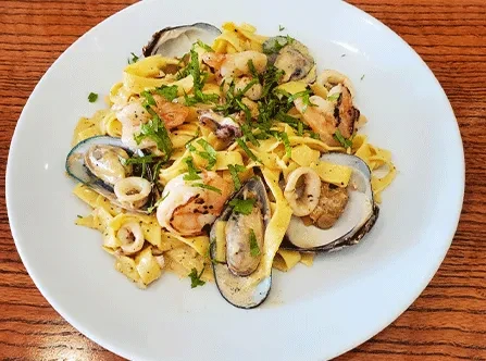 Seafood pasta with mussels, shrimp, calamari, and green herbs.