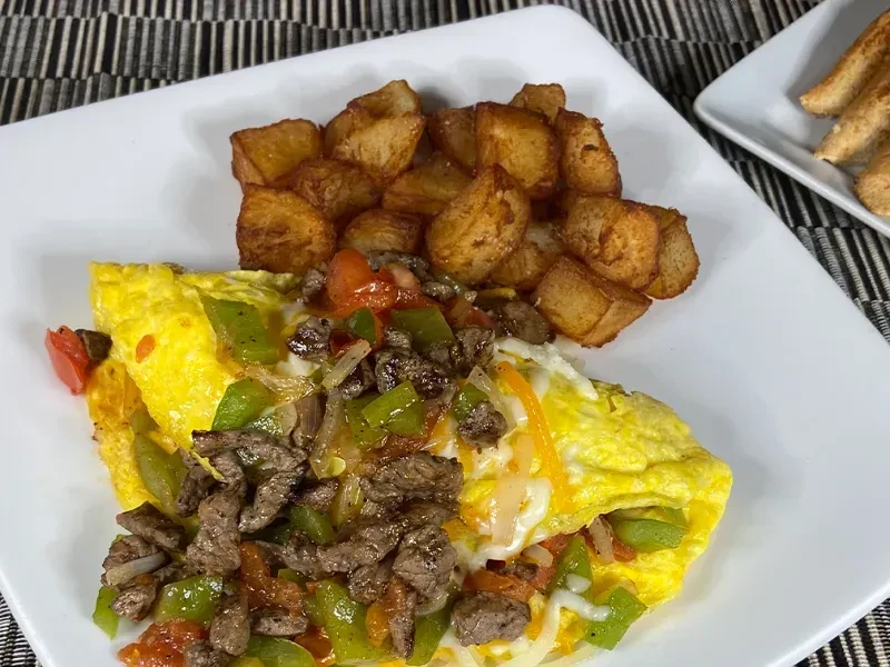 Close-up omelet with steak, vegetables, melted cheese, and home fries.