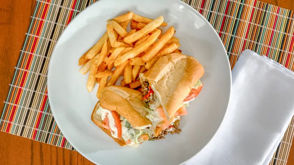 Overhead close-up of a meat sandwich, fries, and striped placemat.