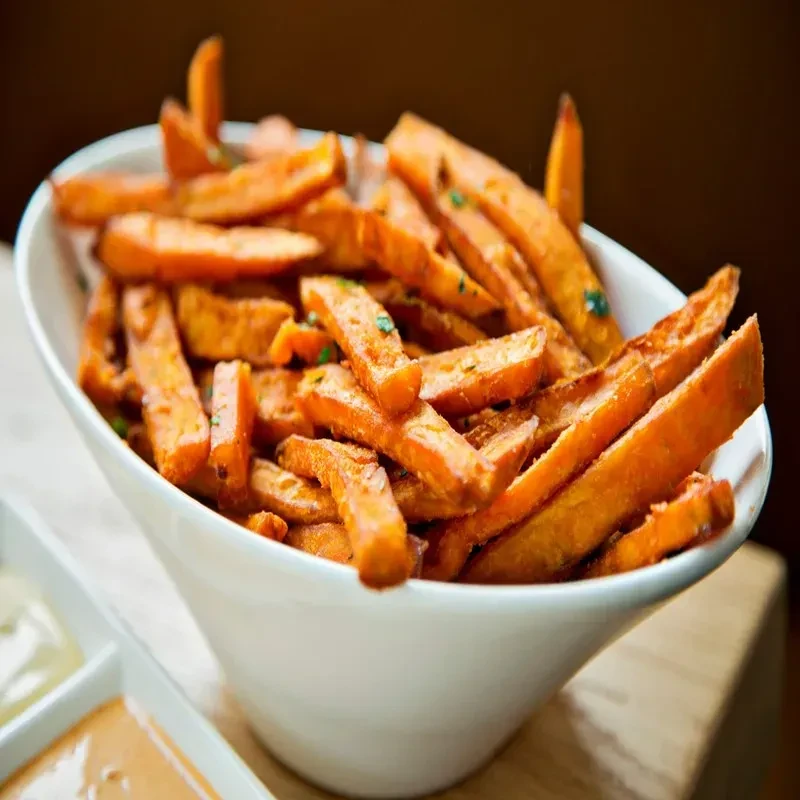 White bowl of crispy sweet potato fries with two dipping sauces.