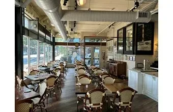 Empty restaurant dining area with modern design, cane chairs, and exposed ducts.