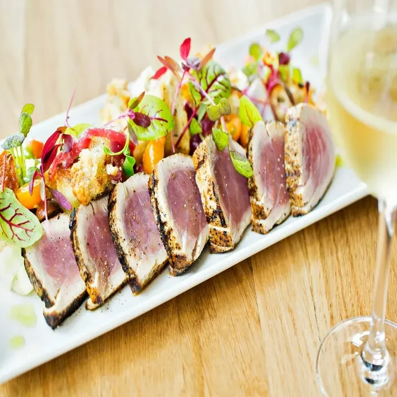 Sliced seared tuna, rare pink, with microgreens, orange, and red accents.