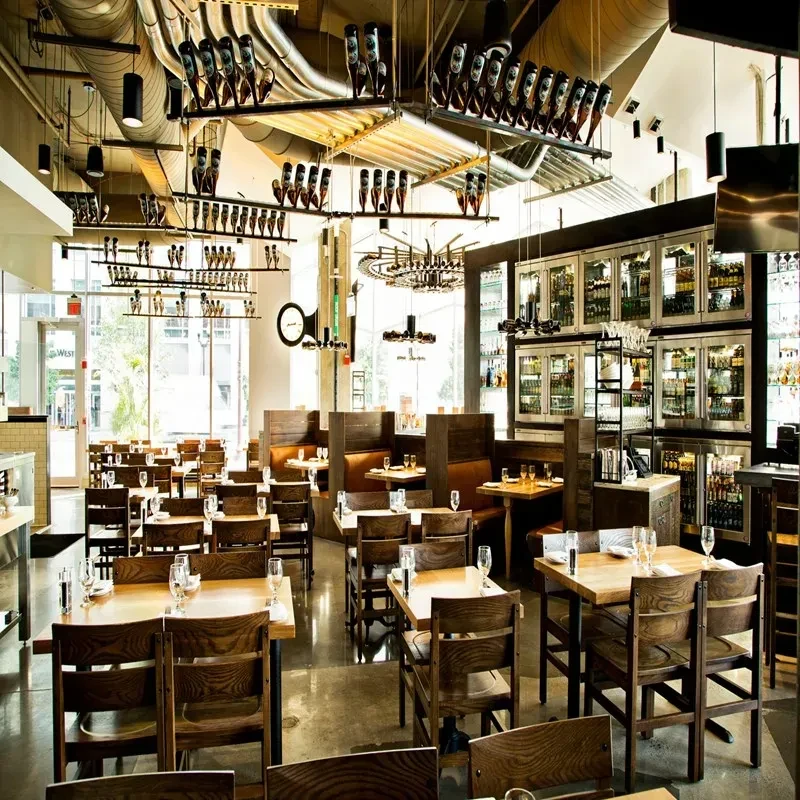 Modern industrial-chic restaurant with dining tables, bar, and unique bottle decor.