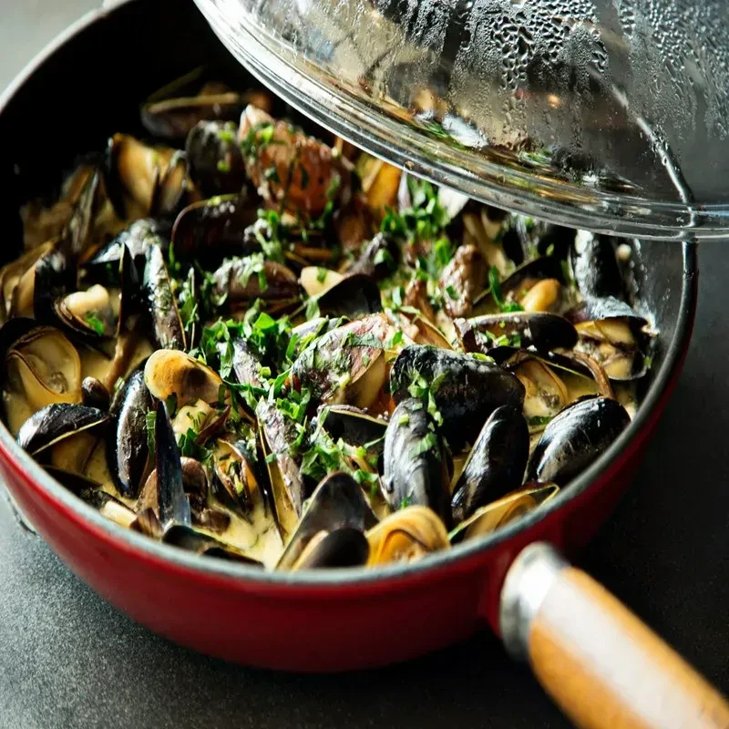 Creamy steamed mussels with green herbs in a vibrant red pan.