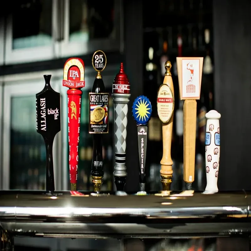 Close-up of nine distinct beer tap handles on a chrome bar rail.