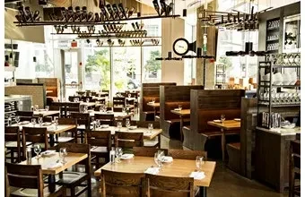 Well-lit modern restaurant interior with wooden tables, booths, and bar.