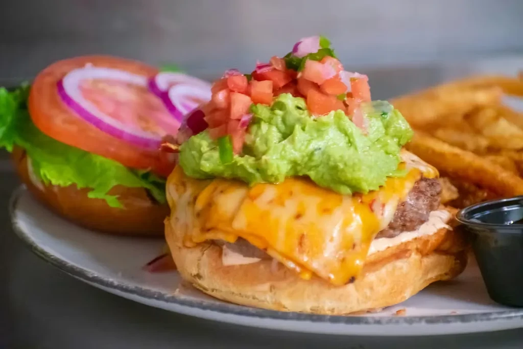 Stacked gourmet burger with melted cheese, guacamole, pico de gallo, fries.