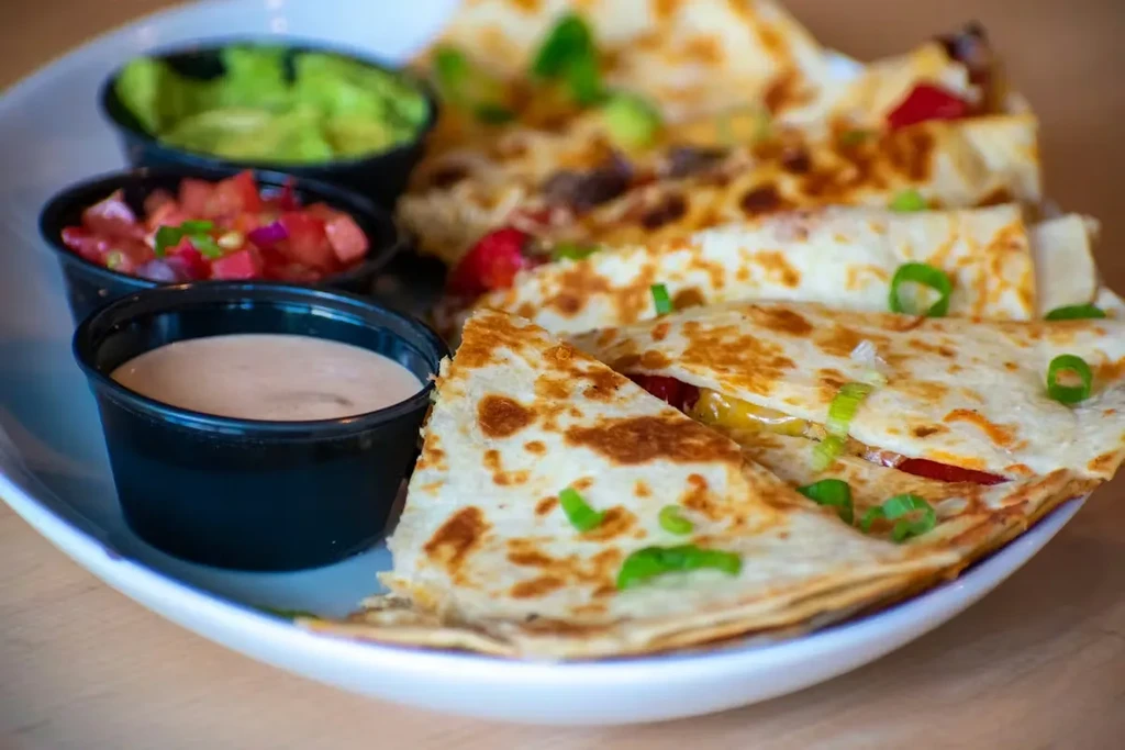 Charred quesadilla wedges, green onions, and three colorful dips on a plate.