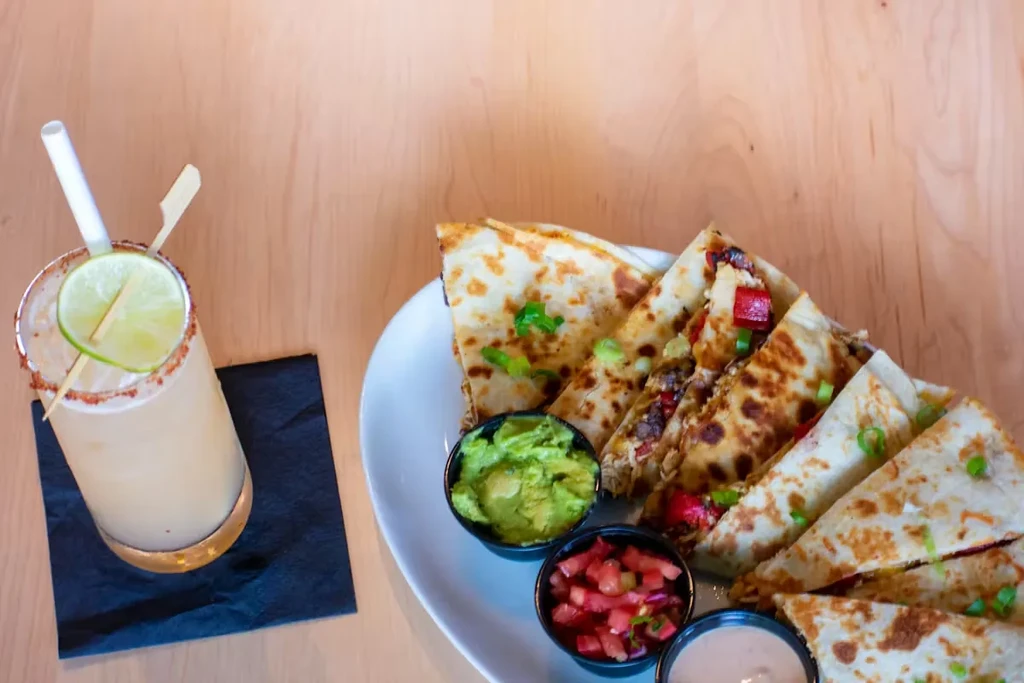 Golden quesadillas with three dips and a drink on a wooden table.