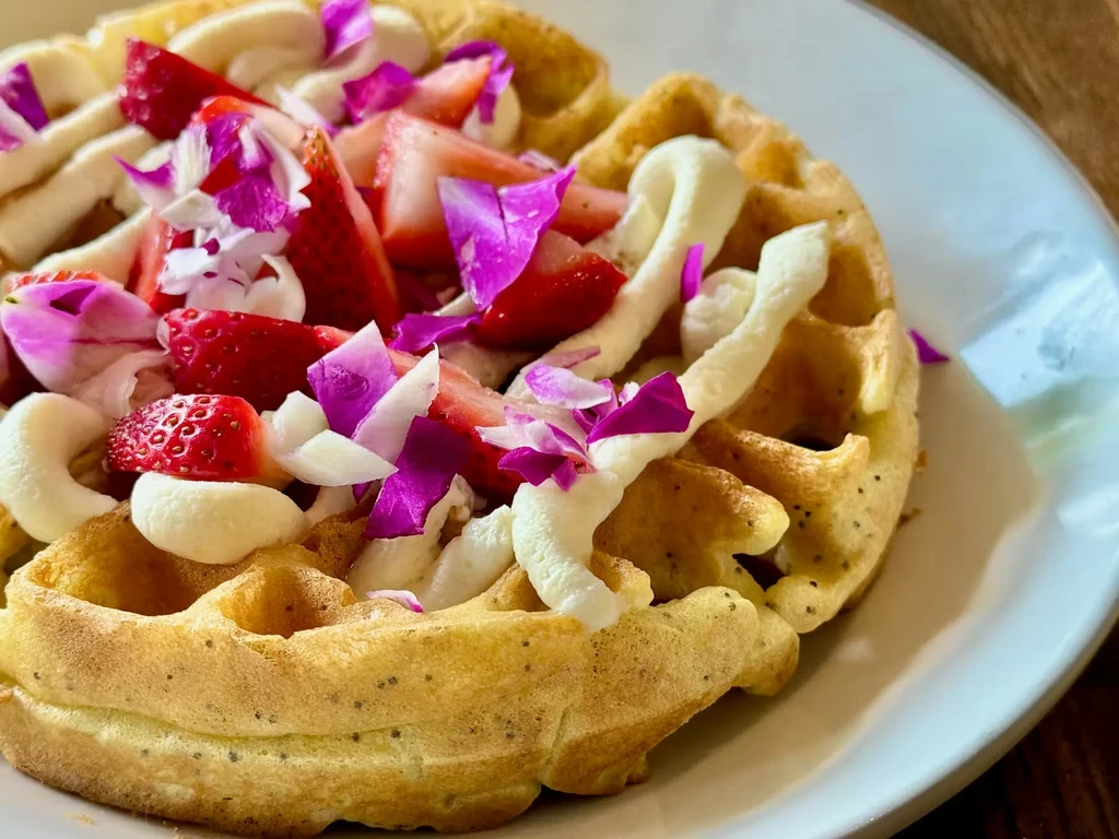 Golden-brown waffle with strawberries, white topping, and edible flower petals.