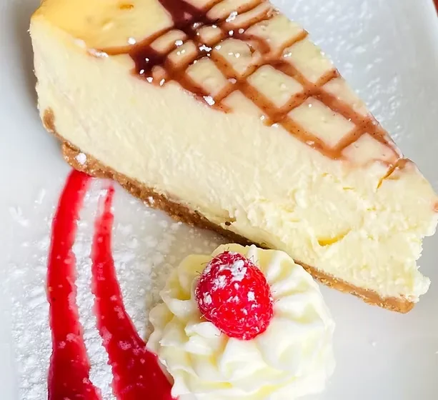 Cheesecake slice with lattice, raspberry, whipped cream, red sauce, powdered sugar.