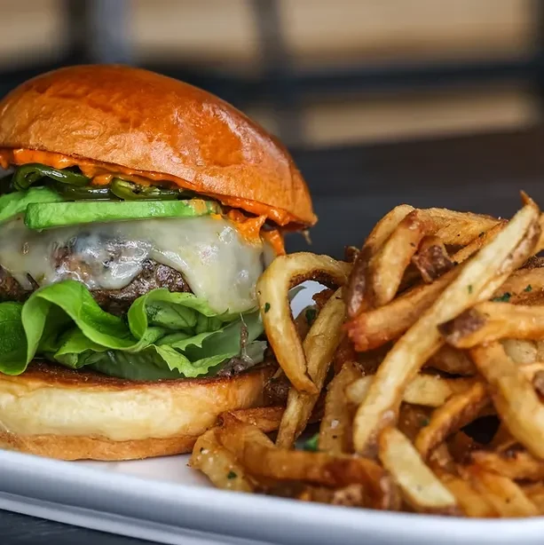 Gourmet burger with avocado, jalapeños, and seasoned French fries.
