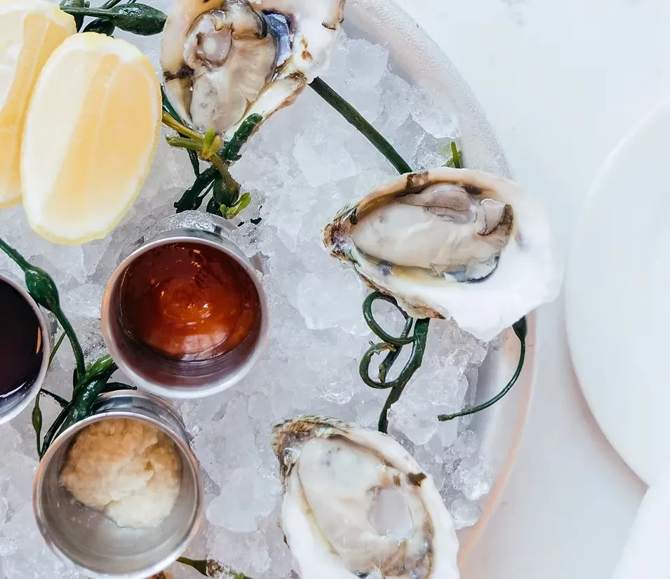 Close-up of shucked oysters on ice with lemon wedges and sauces.