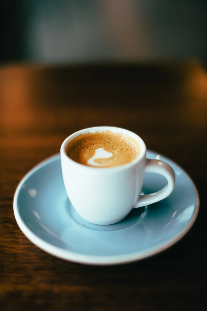 White espresso cup with heart latte art on wooden surface.