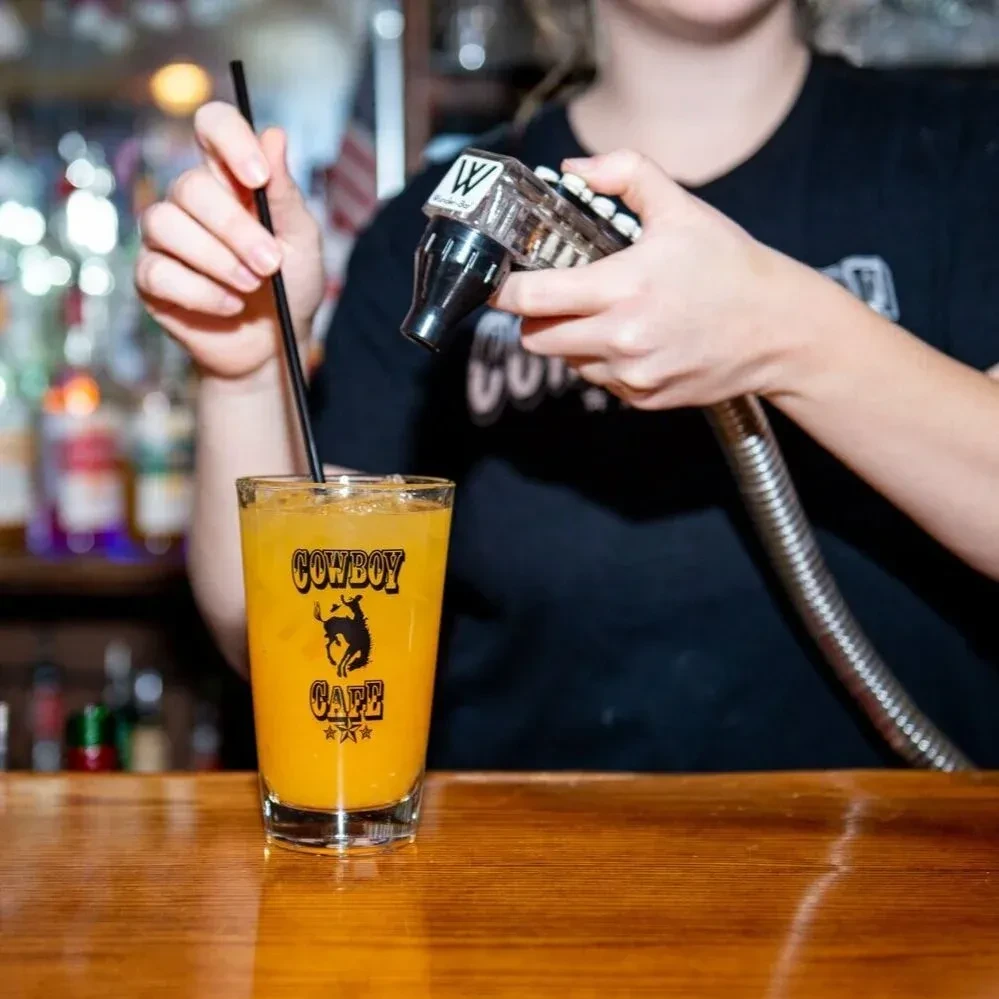 Bartender prepares an orange drink in a Cowboy Cafe branded glass.