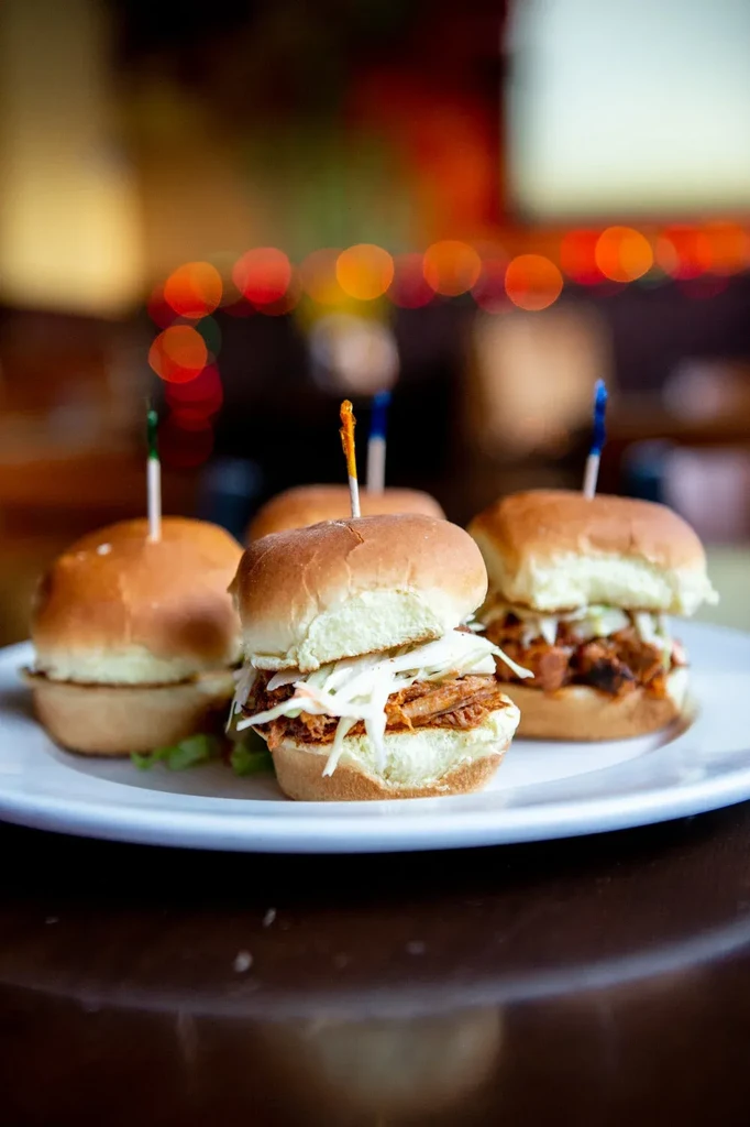 Four pulled meat and coleslaw sliders on a plate.