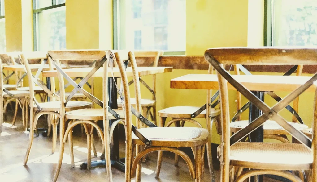 Bright, empty cafe with light wood tables, chairs, and yellow walls.