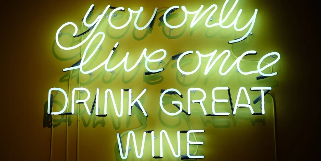 Glowing green neon sign reads "you only live once DRINK GREAT WINE".