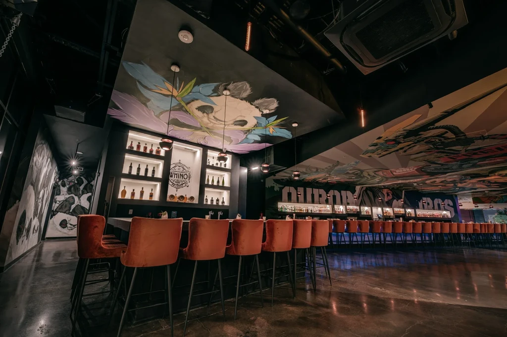 WHINO bar interior with orange stools and colorful fantasy murals.