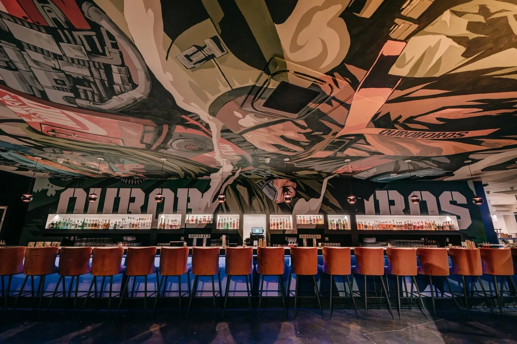 Modern bar interior with orange stools and Ouroboros mural.