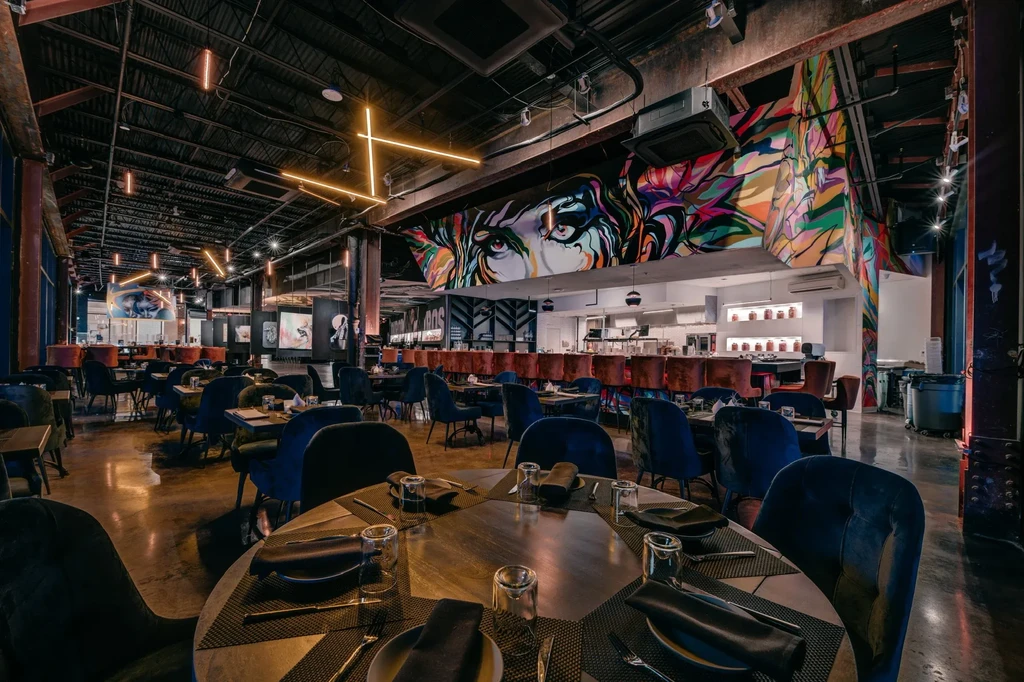 Empty industrial chic restaurant with a colorful eye mural over the bar.