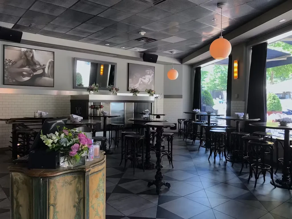 An empty restaurant features a checkered floor, high tables, and eclectic decor.
