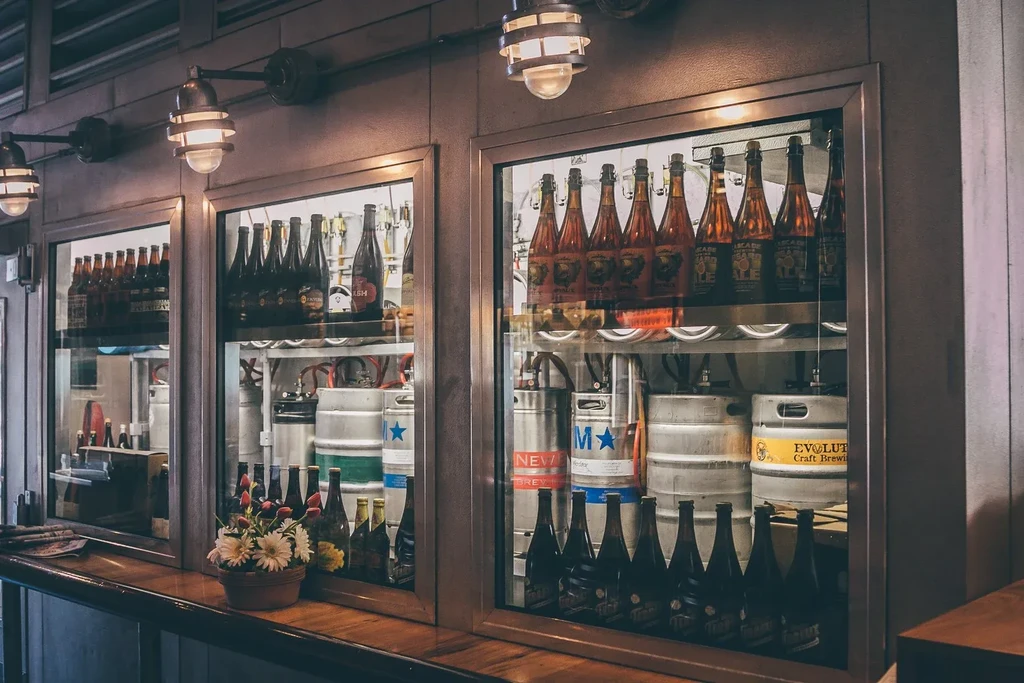 Beer bottles and branded kegs in a refrigerated bar display.