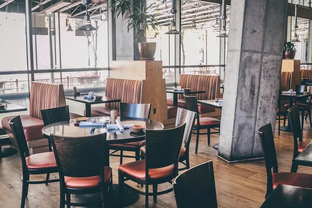 Empty modern restaurant with set tables and red-orange seating.