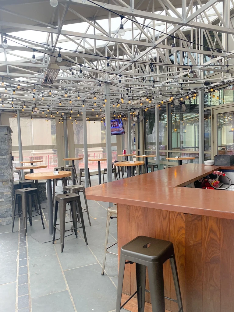 Enclosed restaurant patio with bar, high-top tables, and overhead string lights.