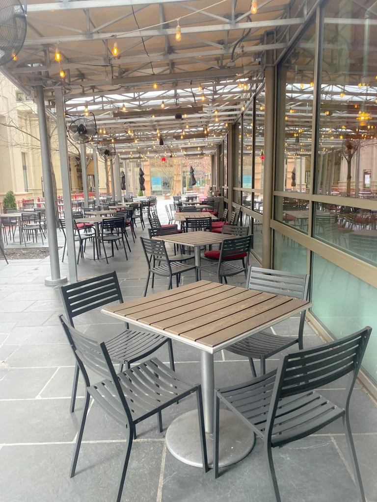 Modern outdoor restaurant patio with empty tables under a lit canopy.