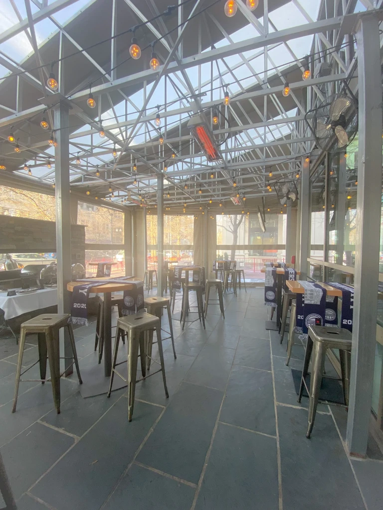 Covered patio with glass roof, string lights, and high-top tables.