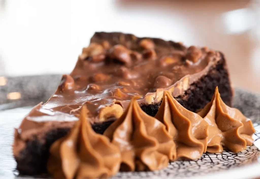 Chocolate dessert slice with nuts and caramel swirls on white plate.