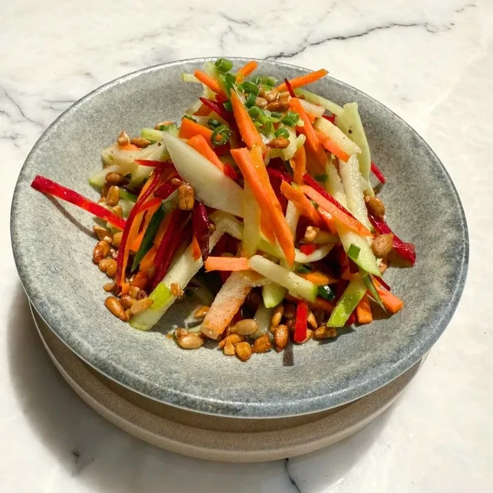 Vibrant julienned vegetable salad with peanuts in a ceramic bowl.