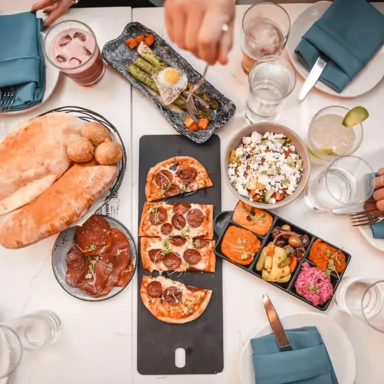 Overhead view of a dining table with diverse food, drinks, and diners.