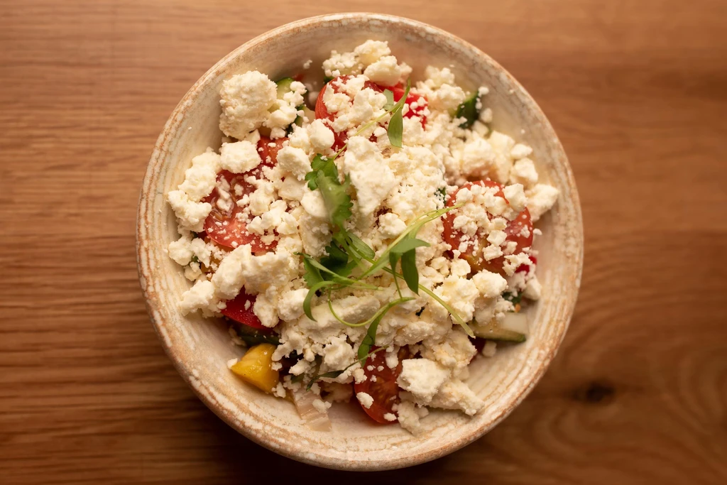 Overhead: Rustic bowl of salad with crumbled feta, tomatoes, and herbs.