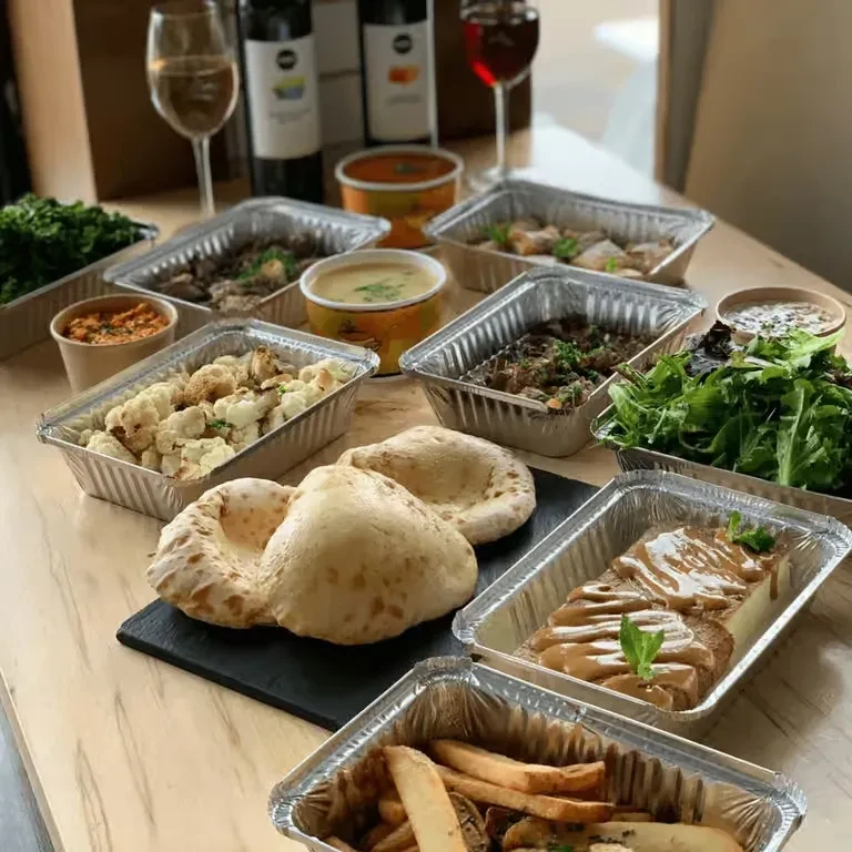 Overhead view of a wooden table with various takeout food and wine.