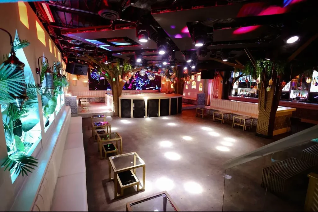 Empty modern nightclub with lounge seating, stage, bar, and colorful lights.