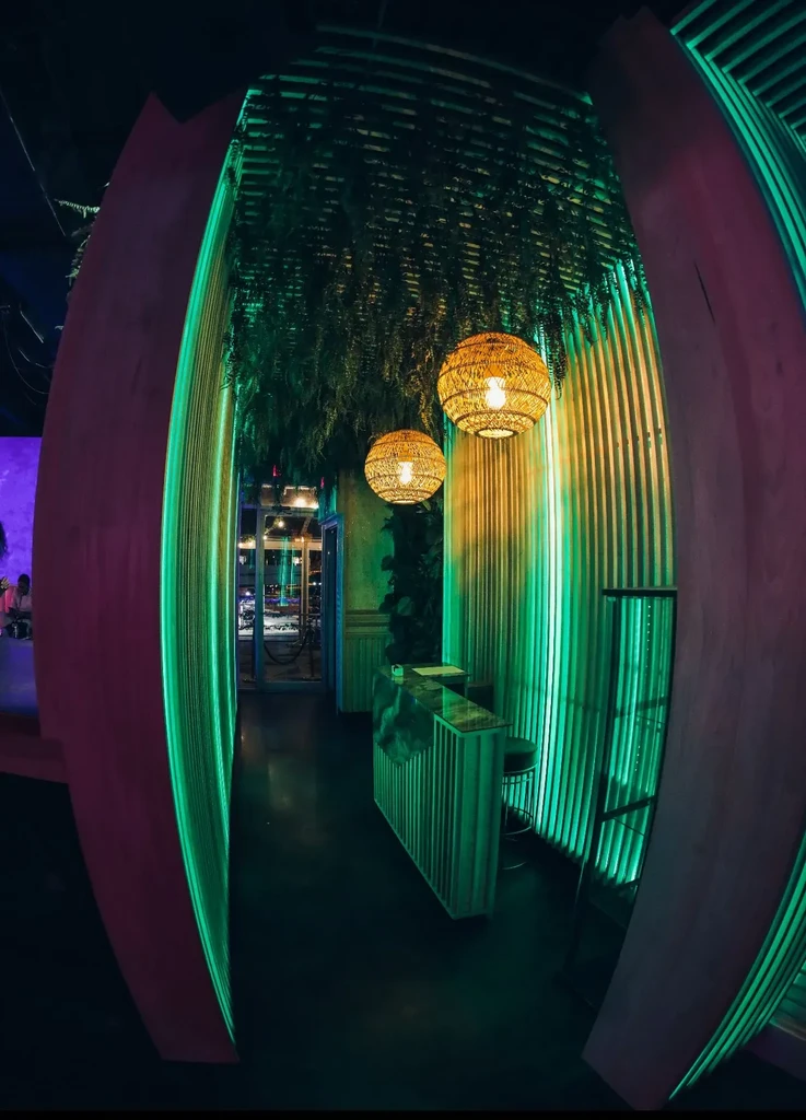 Arched corridor with green LED lighting, foliage ceiling, and reception stand.