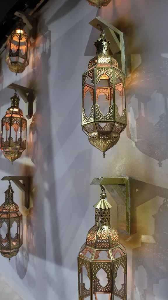 Multiple ornate brass lanterns on a wall emitting warm patterned light.