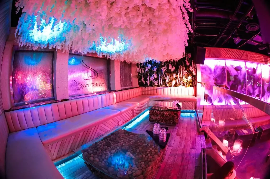 Lounge with plush pink seating, hanging florals, and colorful LED lighting.