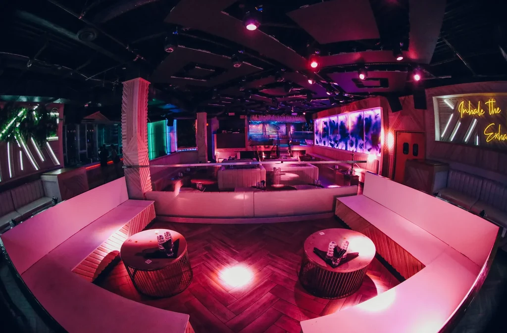 Wide-angle view of a vibrant bar interior with colorful neon lights.