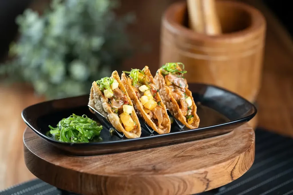 Three crispy tacos with protein, pineapple, and green seaweed salad.