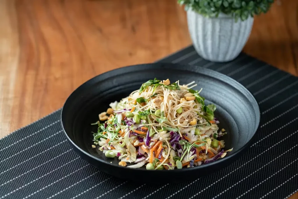 Colorful vermicelli salad with vegetables and peanuts in black bowl.