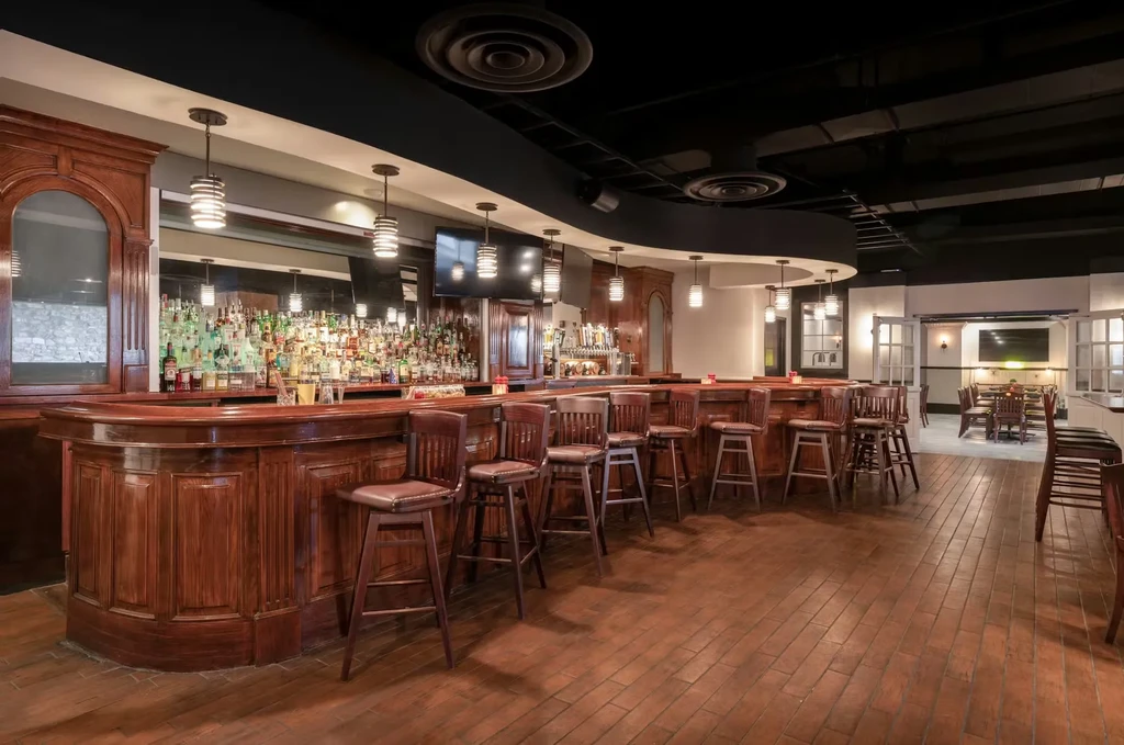 Empty, well-lit dark wood bar with stools and mirrored liquor display.