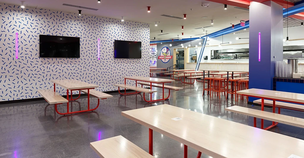 Modern restaurant interior with picnic tables, colorful walls, and red accents.