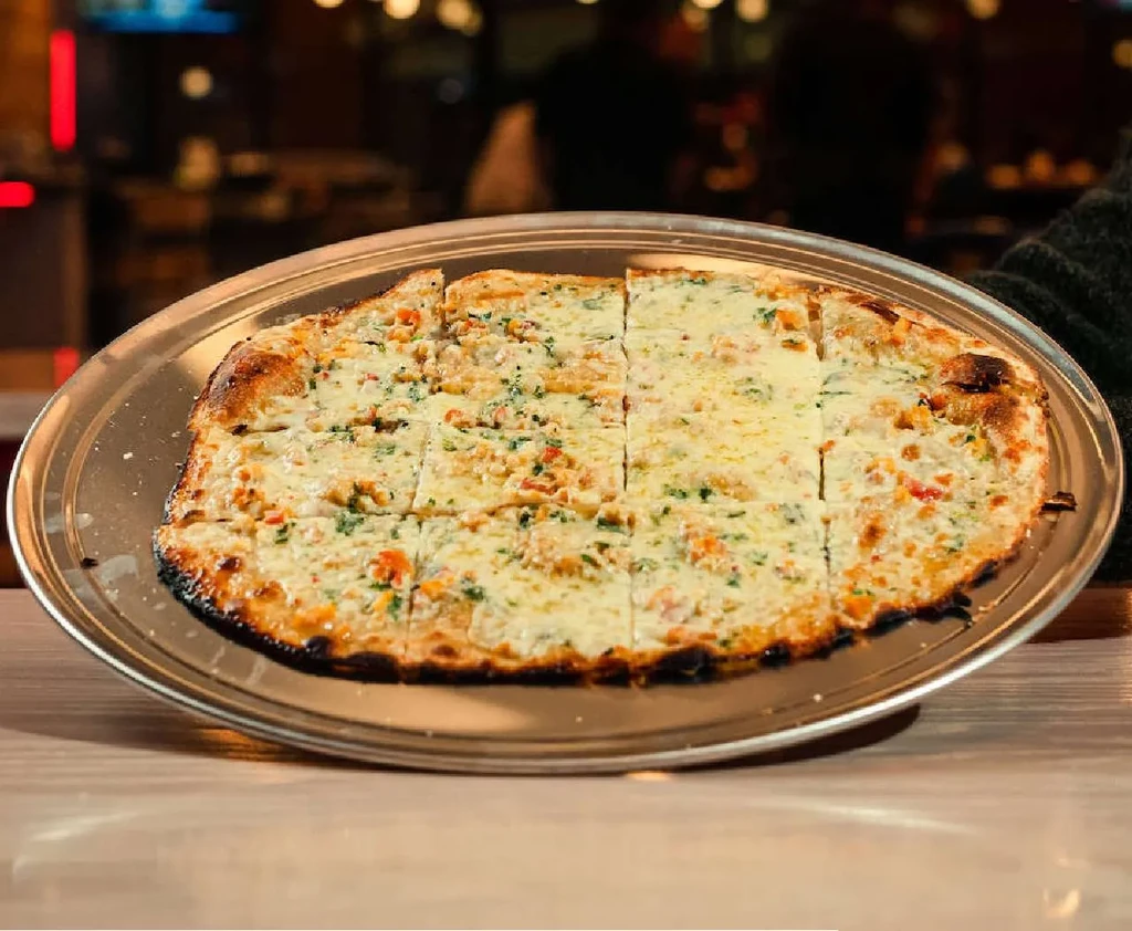 Flatbread pizza with cheese, herbs, and toppings on a silver pan.