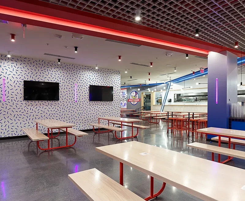Modern restaurant with red/blue decor, picnic tables, and a "Night-Snake Burgers" sign.
