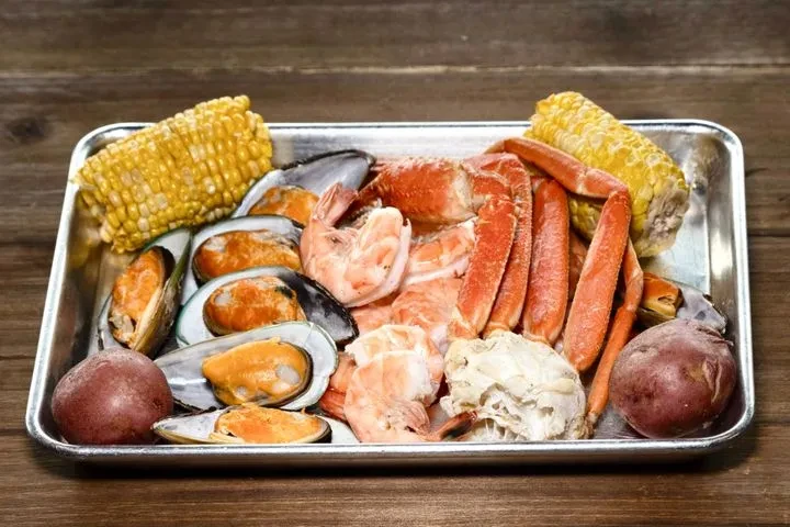 Cooked seafood platter with crab, shrimp, mussels, corn, and potatoes.
