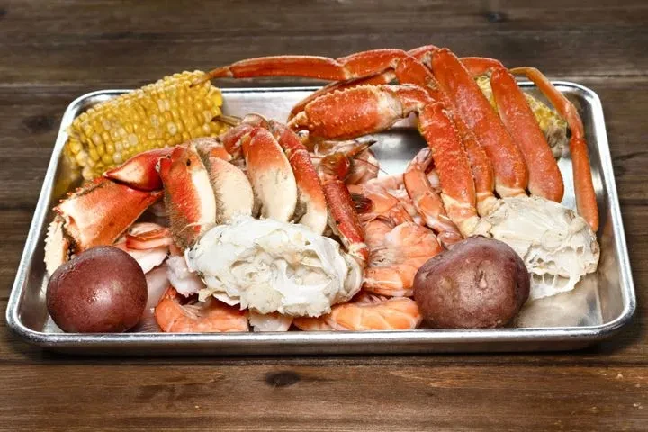 Cooked seafood platter on a tray, with crab, shrimp, corn, potatoes.