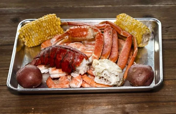 Cooked lobster, crab, shrimp, corn, and potatoes on a silver tray.